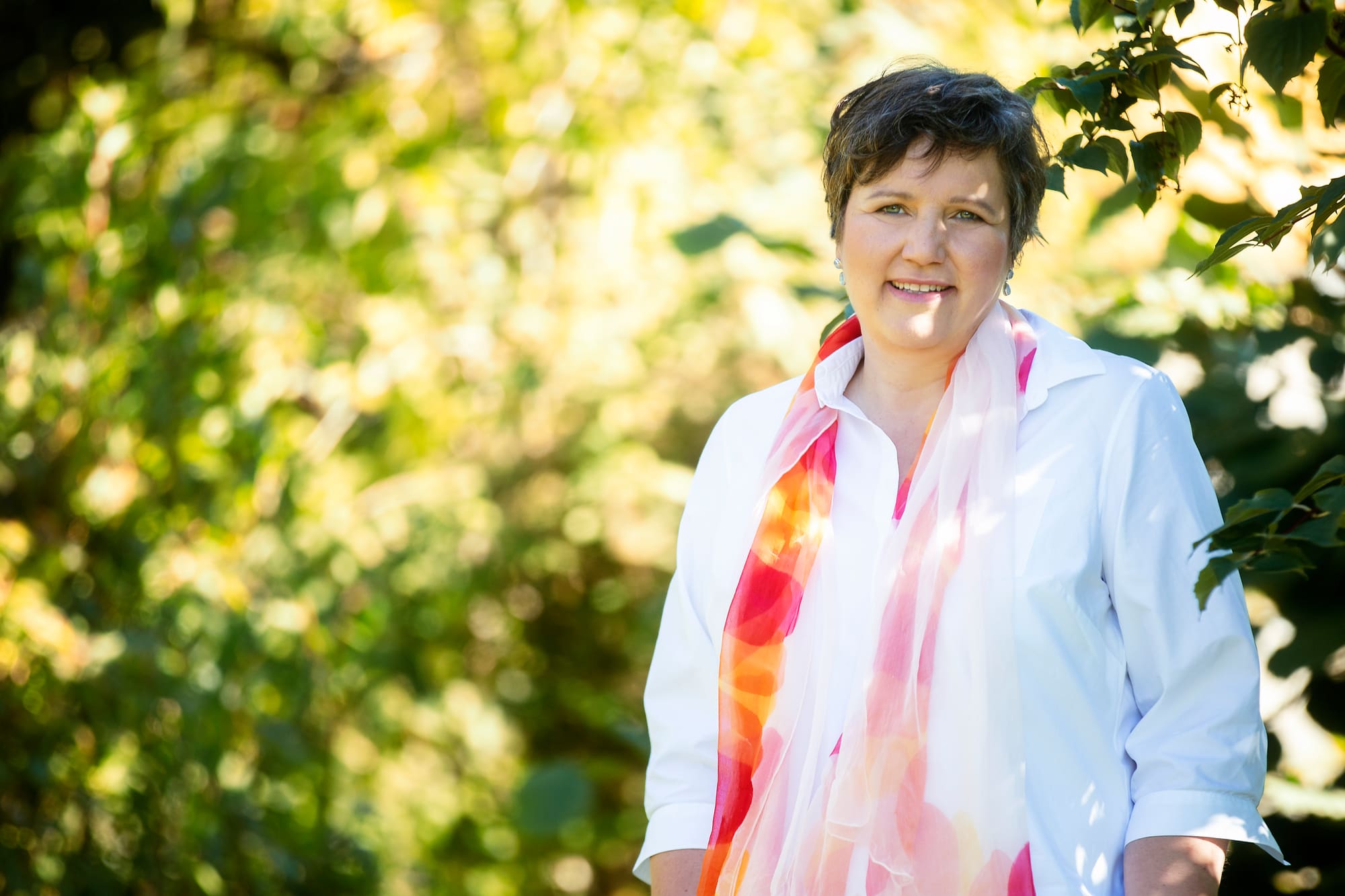 Gabriele Kirchmann, lächelnd in sonnigem Grün, mit weißer Bluse und buntem Seidenschal